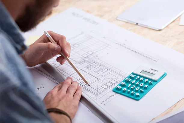 Man looking over a blueprint on the table with a ruler and calculator