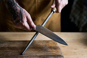 Man with tattoos on his hands sharpening a knife