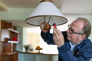 An older gentleman wearing glasses repairing a lamp with a screwdriver