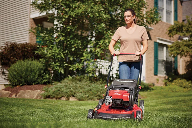 Woman wearing clear safety glasses while using a push lawn mower to mow the lawn