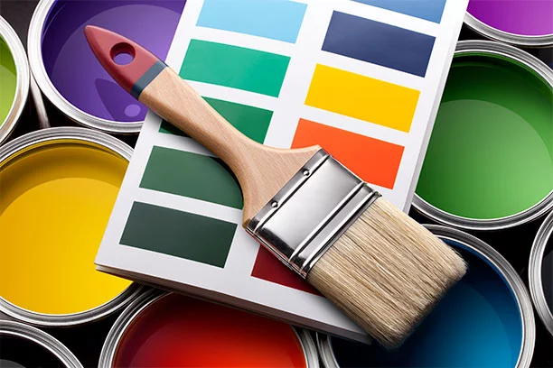 A paint brush and paint color swatches laying on top of open paint cans