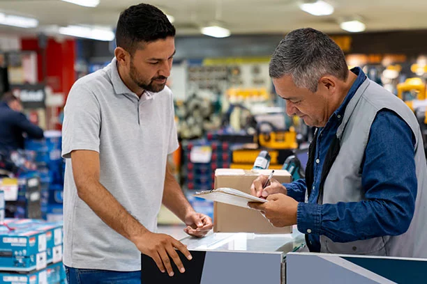 A man in a hardware store talking to an employee at the counter