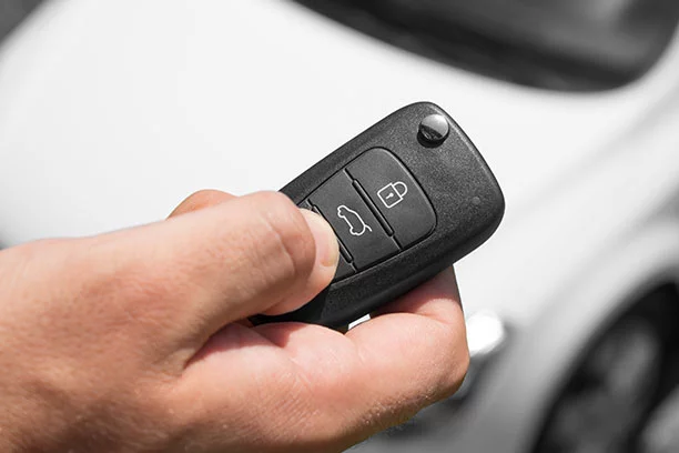 Person holding a key fob in the foreground with a white car blurred in the background