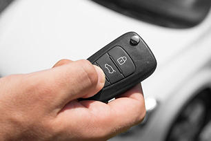 Person holding a key fob in the foreground with a blurred vehicle in the background