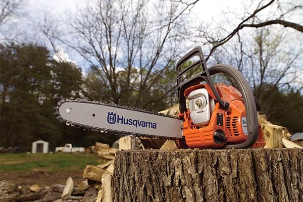 Husqvarna orange and silver chainsaw sitting on a wood stump in a yard 