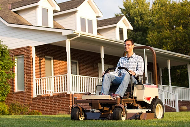 Man riding a Grass Hopper mower in front of a home