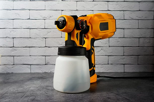 yellow and black paint sprayer in front of a white brick wall