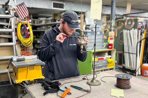 An older man wearing glasses using a welder to fix a hanging light fixture