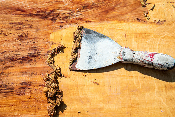 A paint scraper scraping away wood stain pulled up with a chemical stripper