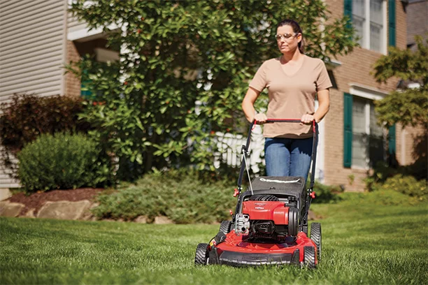 Middle aged woman using a red push mower to mow her front lawn 