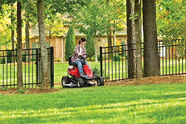 A woman riding a rear engined red riding lawn mower, cutting her grass 