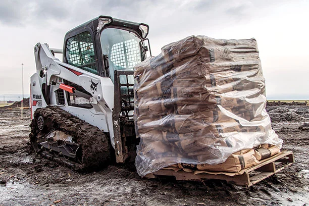Skid steer with a pallet of plastic wrapped bags