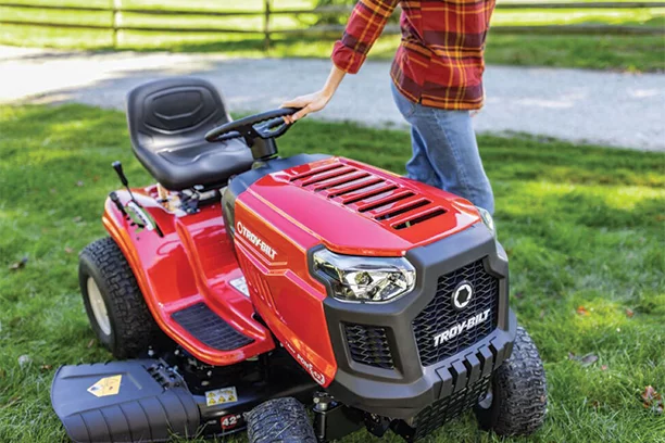 Red and black riding lawn mower sitting in a yard with a woman's hand on the steering wheel 