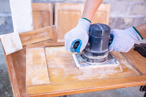 Person wearing work gloves sanding down a kitchen cabinet door outside with a sander