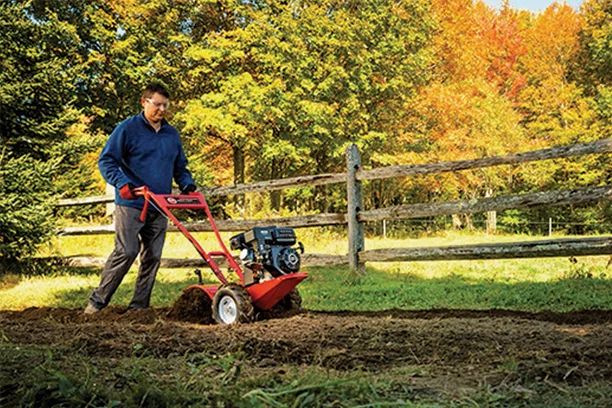 Man pushing a red gas powered tiller in a yard clearing the ground for a garden 