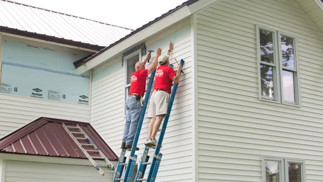 Two Valu volunteers on ladders putting up siding