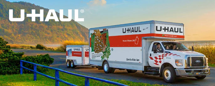 U-Haul truck and trailer driving down the road with a scenic landscape in the background