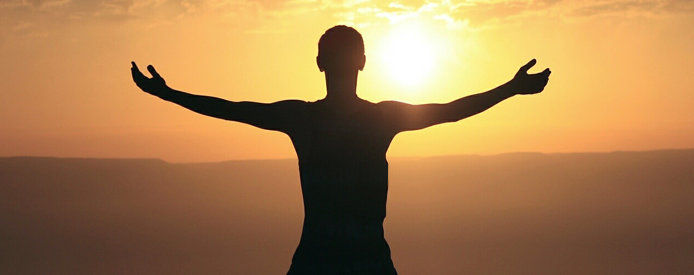 A person holding out their arms facing a sunset