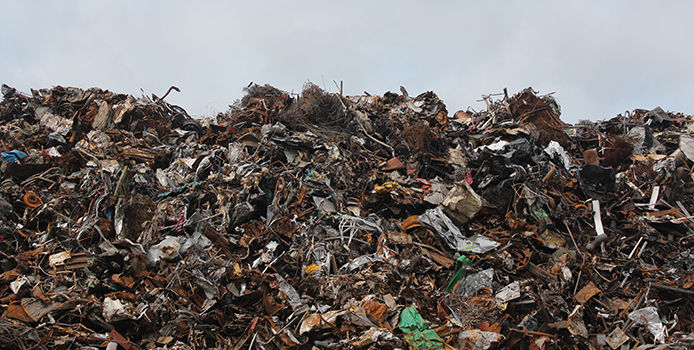 A picture of a full landfill with a blue-grey sky in the background. The landfill shows many pieces of brown, grey, and green debris piled up.