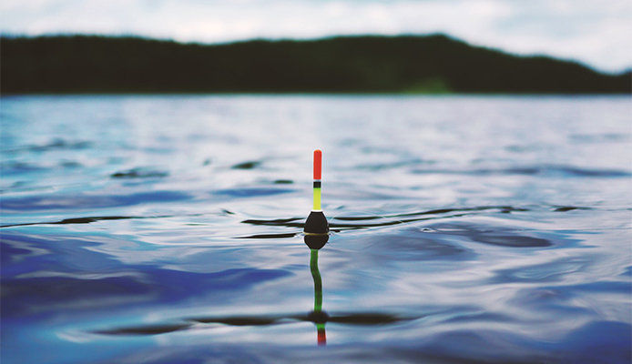 A neon orange and yellow bobber floats atop a blue waterway.