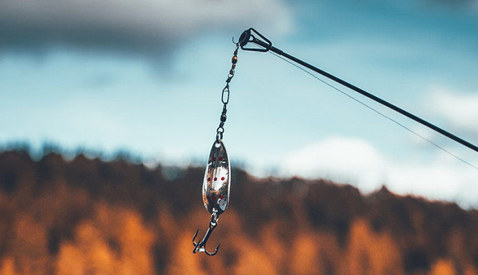 A fishing rod stands out against an aqua-blue and orange skyline. A silver lure and hook hang from the line.