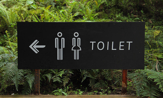 A black and white sign with an outline of a man and woman with an arrow pointing to the toilets