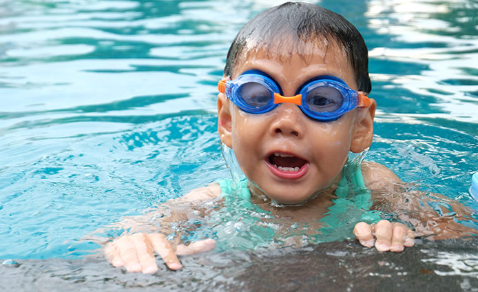 A young boy wearing goggles and swimming in a pool