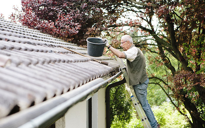 Man standing on a ladder with a bucket in hand cleaning out his gutters