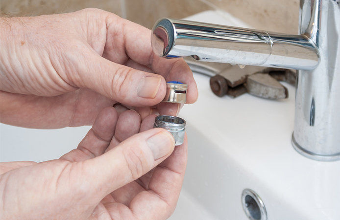 A person is removing the bottom part of a silver faucet. In their fingers, they are holding the washer that fits beneath the screen of the tap.