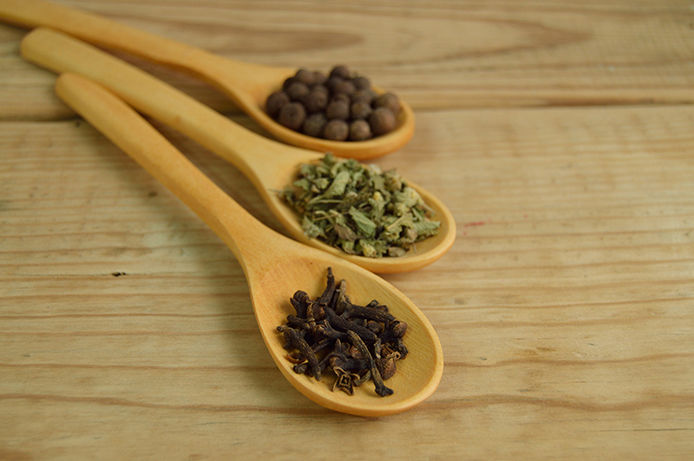 Three wooden spoons with different herbs/spices in each on wooden tabletop