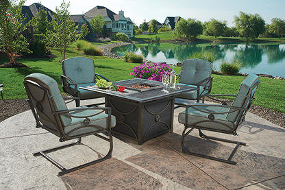five piece patio set with a fire pit table sitting on a stone patio and a pond in the background 