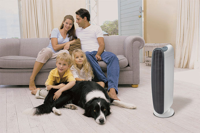 A family of four and a dog sitting on a couch in a living room with a portable fan next to them