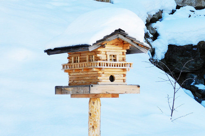 A wooden 2-story bird house with snow on its roof