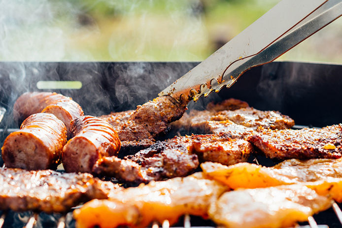 Close up image of a charcoal grill, grilling sausage, chicken, and ribs 