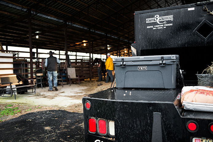 Featuring a YETI cooler sitting on the back of a flatbed pickup truck with a cow barn in the background