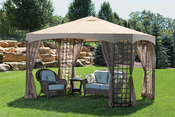 A perogla sitting on a grassy lawn with a three piece wicker patio set under it and with blue cushion
