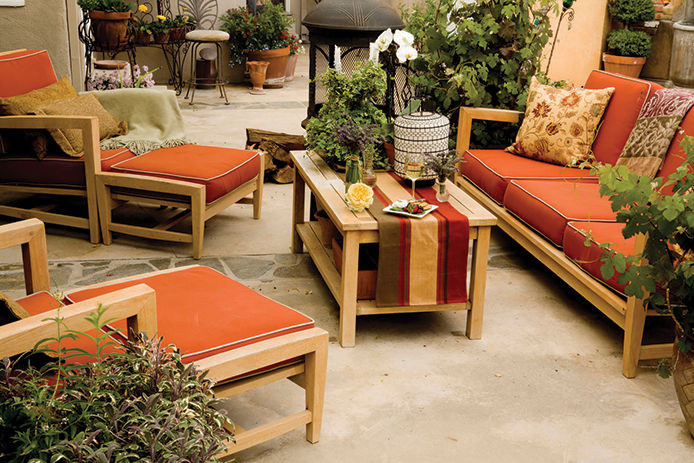 Wooden patio furniture set with red cushion and greenery surrounding the patio 