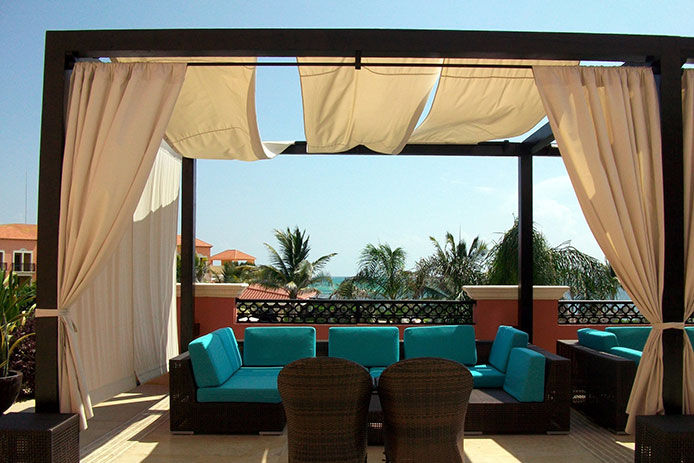 Beautiful patio on the west coast by the ocean with palm trees in the background. There is a wooden pergola with canvas sheets drapping over the sides 