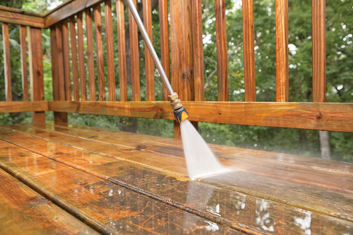 A close up of a pressure washer cleaning grime off of a wooden deck