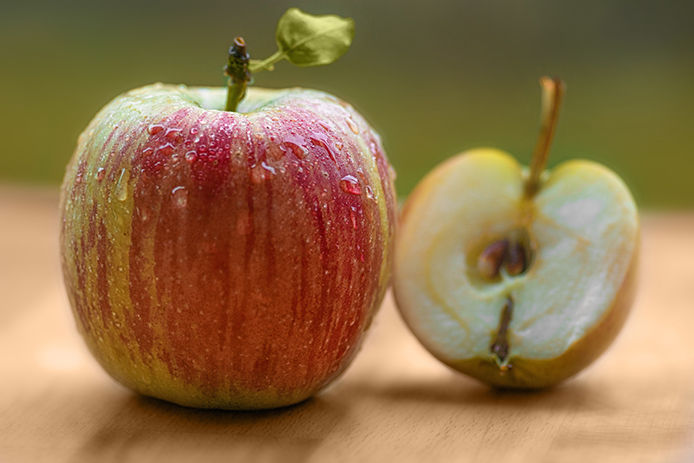 An apple on a wooden tabletop with a half cut open apple beside it
