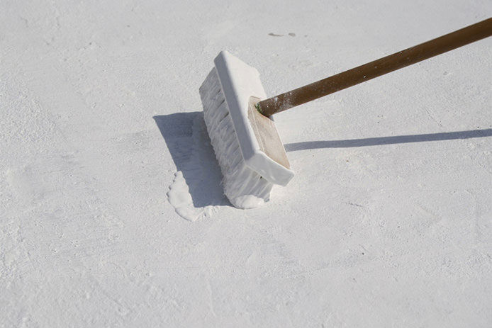 Applying a thick white coating of roof coating on a rooftop