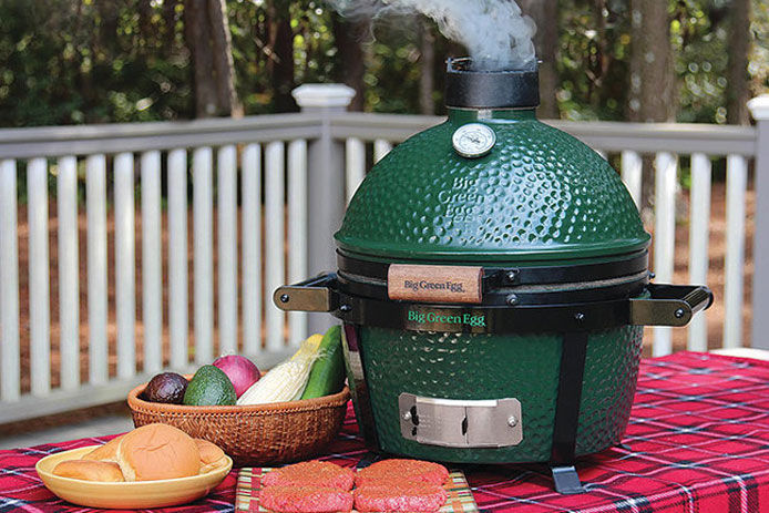 Big Green Minimax Egg with Carrier sitting on a picnic table with burgers and veggies
