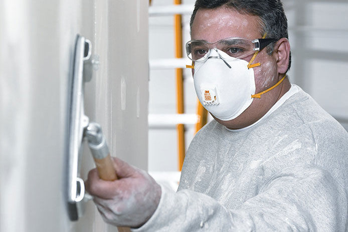 A professional contractor wearing a N95 mask using a pole brush and sanding the wall