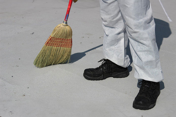 a man wearing black shoes and white coverall using a broom to sweep up debris on a rooftop
