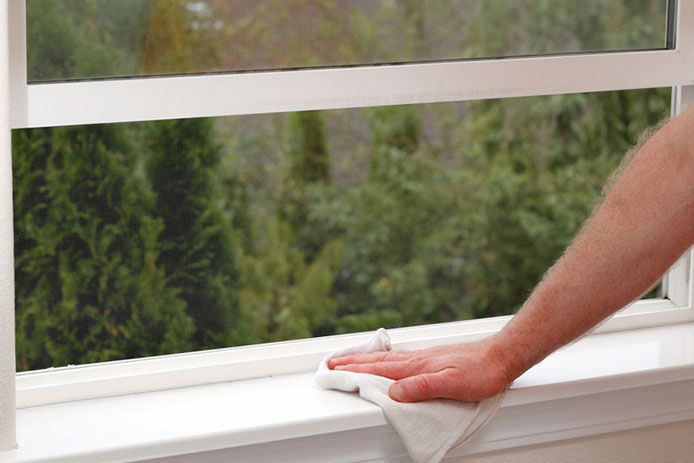 A close up image of a hand holding a cloth to clean and wipe down a white window sill