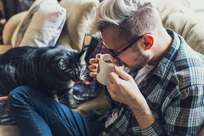 Man inside drinking coffee with his cat
