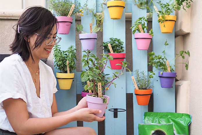 woman by a virticle Herb garden of small pots attached to a fence