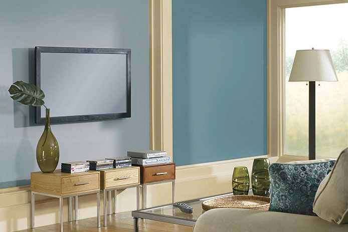 A modern family room with teal blue walls and a tv hanging in front of a white couch 