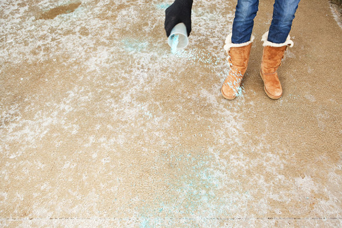 Person spreading ice melt on concrete with plastic cup