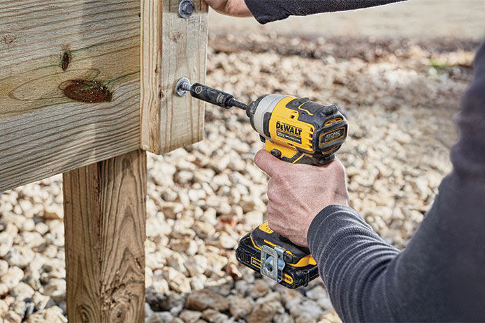 Person using a DEWALT ATOMIC 20V MAX Brushless 1/4 In. Compact Cordless Impact Driver to drive a bolt into a wooden post